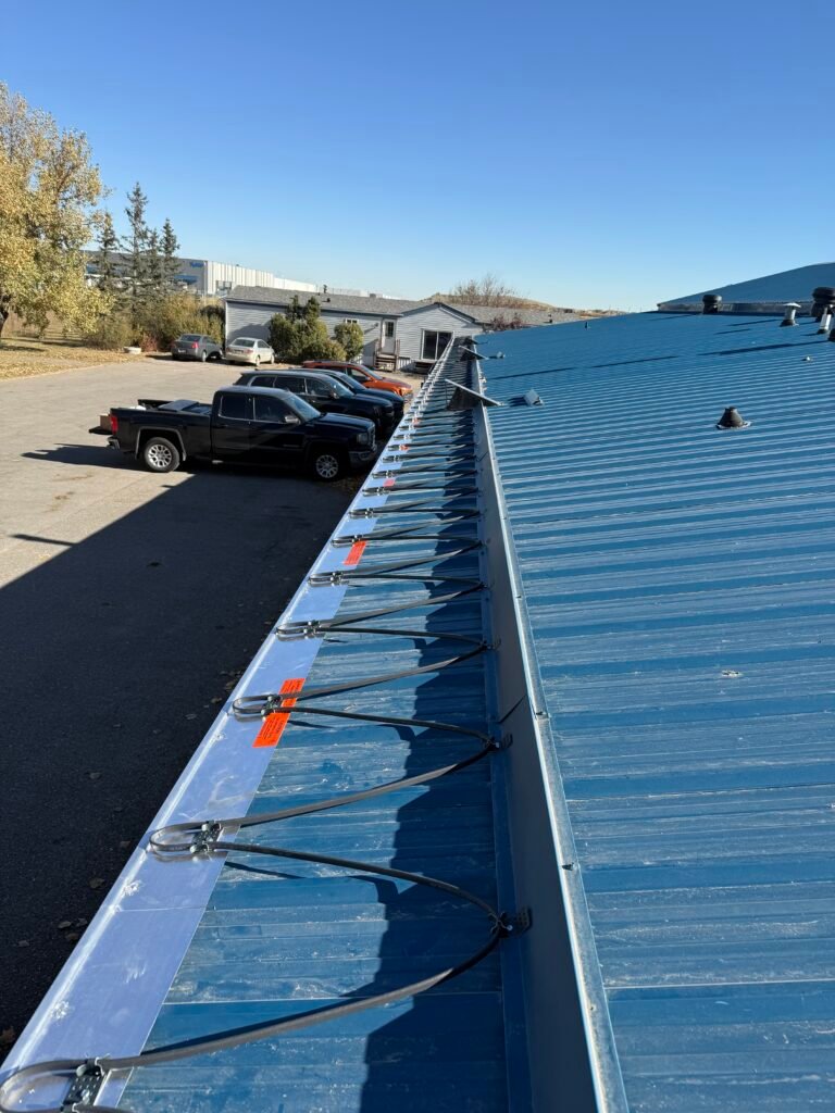 Commercial metal roof de-icing cable system installation with heavy-duty mounting clips on a blue industrial roof.