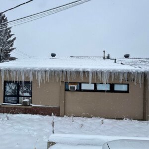 Severe commercial building icicle formation and heavy ice loading along a roofline before professional de-icing.