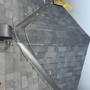 Close-up of residential roof de-icing cables secured with heavy-duty clips down an asphalt shingle ridge and valley.