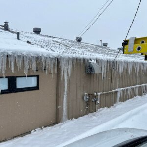 Severe icicle formation and commercial roof ice damming on an industrial building before heat cable installation.